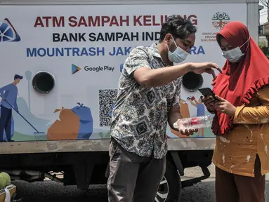 Petugas mendampingi warga saat memindai sampah botol melalui aplikasi smartphone sebelum ditabung ke ATM Sampah Keliling di kawasan Semper Barat, Cilincing, Jakarta Utara, Selasa (12/10/2021). (merdeka.com/Iqbal S. Nugroho)