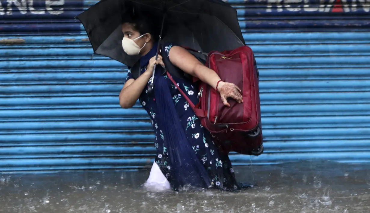 Seorang wanita mengenakan masker sebagai tindakan pencegahan terhadap virus corona melintasi banjir saat hujan lebat di Mumbai, India, Rabu, (5/8/2020). Musim hujan India berlangsung dari Juni hingga September. (AP Photo/Rajanish Kakade)