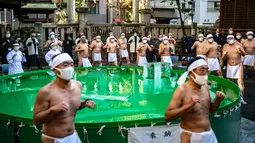 Penganut Shinto dari Kuil Teppozu Inari melakukan pemanasan sebelum mandi dengan air dingin untuk pemurnian jiwa selama ritual Tahun Baru di Tokyo, Jepang, Minggu (9/1/2022). Sejumlah pria mengenakan cawat tradisional dan wanita dengan jubah putih mengikuti ritual tersebut. (Philip FONG/AFP)