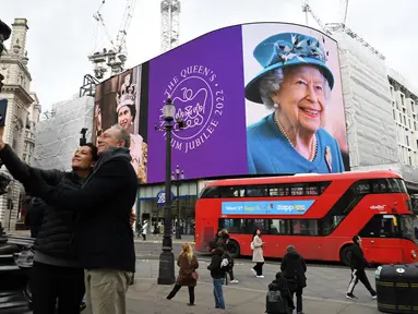 Pasangan berfoto saat bus London merah lewat, di mana gambar Ratu Elizabeth II ditampilkan pada layar digital besar untuk menandai dimulainya Platinum Jubilee di Piccadilly Circus, 6 Februari 2022. Ratu Elizabeth II menjadi raja Inggris pertama yang memerintah selama tujuh dekade. (Daniel LEAL/AFP)