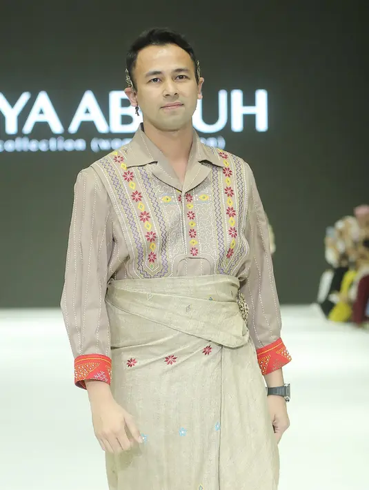 Menyusul sang istri di belakangnya, Raffi Ahmad tampak memesona mengenakan kemeja dan kain berwarna nude dengan corak ulos.  [Fimela/Bambang E. Ros]