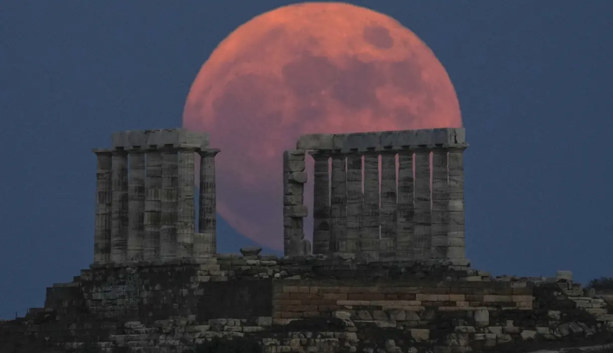 Bulan Purnama Stroberi atau Strawberry Full Moon muncul di belakang Kuil Poseidon marmer kuno di Cape Sounion, sekitar 70 Km selatan kota Athena, Yunani, Kamis (24/6/2021). Julukan ini disematkan oleh suku asli Amerika yang dipopulerkan dalam Farmers Almanac. (AP Photo/Petros Giannakouris)