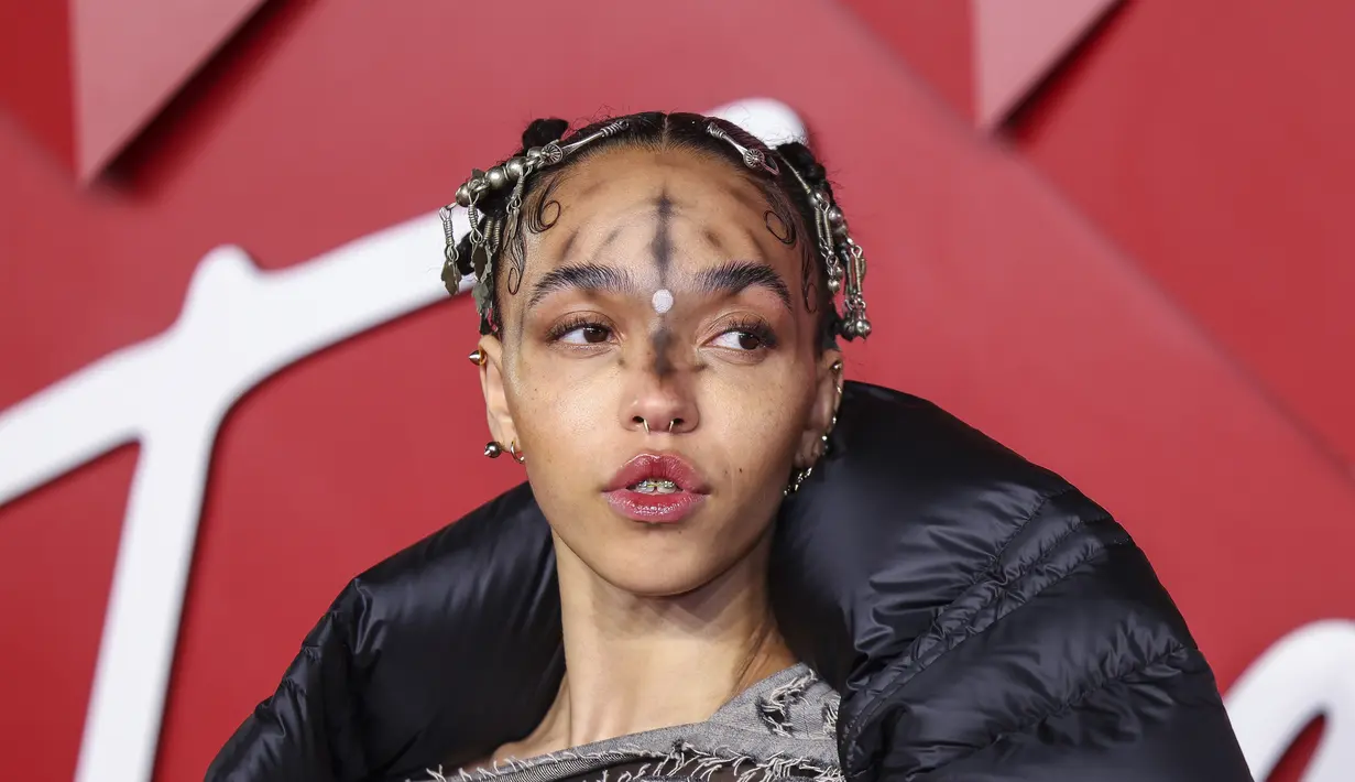 FKA Twigs berpose untuk fotografer setibanya di British Fashion Awards di London, Senin, 5 Desember 2022. Gaunnya menampilkan panel garis tipis dari bahan berjumbai yang menambahkan beberapa dimensi padanya.Dia menyelipkan kakinya ke dalam sepasang tumit platform hitam dan abu-abu yang menambahkan beberapa inci ke tubuhnya. (Photo by Vianney Le Caer/Invision/AP)