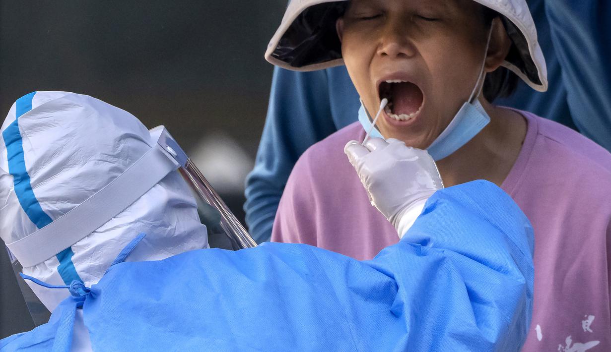 <p>Seorang pekerja yang mengenakan pakaian pelindung menyeka tenggorokan seorang wanita untuk tes COVID-19 pada hari ketiga berturut-turut tes virus corona massal di Beijing, Kamis (5/5/2022). Ibu kota China Beijing pada Kamis (5/5) mulai melonggarkan aturan karantina untuk kedatangan dari luar negeri. (AP Photo/Mark Schiefelbein)</p>
