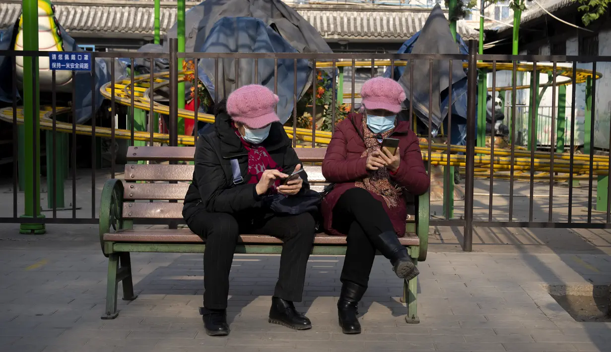 Wanita memakai masker untuk melindungi diri dari COVID-19 melihat smartphone mereka di taman umum di Beijing, Rabu (5/1/2022). China melaporkan penurunan besar infeksi COVID-19 lokal di kota utara Xi'an, yang telah dikunci ketat selama dua minggu terakhir. (AP Photo/Mark Schiefelbein)