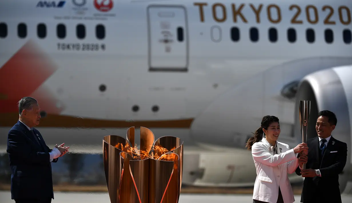 Presiden Olimpiade Tokyo 2020, Yoshiro Mori, menyaksikan dua atlet peraih tiga kali medali emas olimpiade Tadahiro Nomura dan Saori Yoshida menyalakan obor Olimpiade saat tiba dari Yunani di Pangkalan Udara Matsushima, Jepang, Jumat (20/3). (AFP/Philip Fong)
