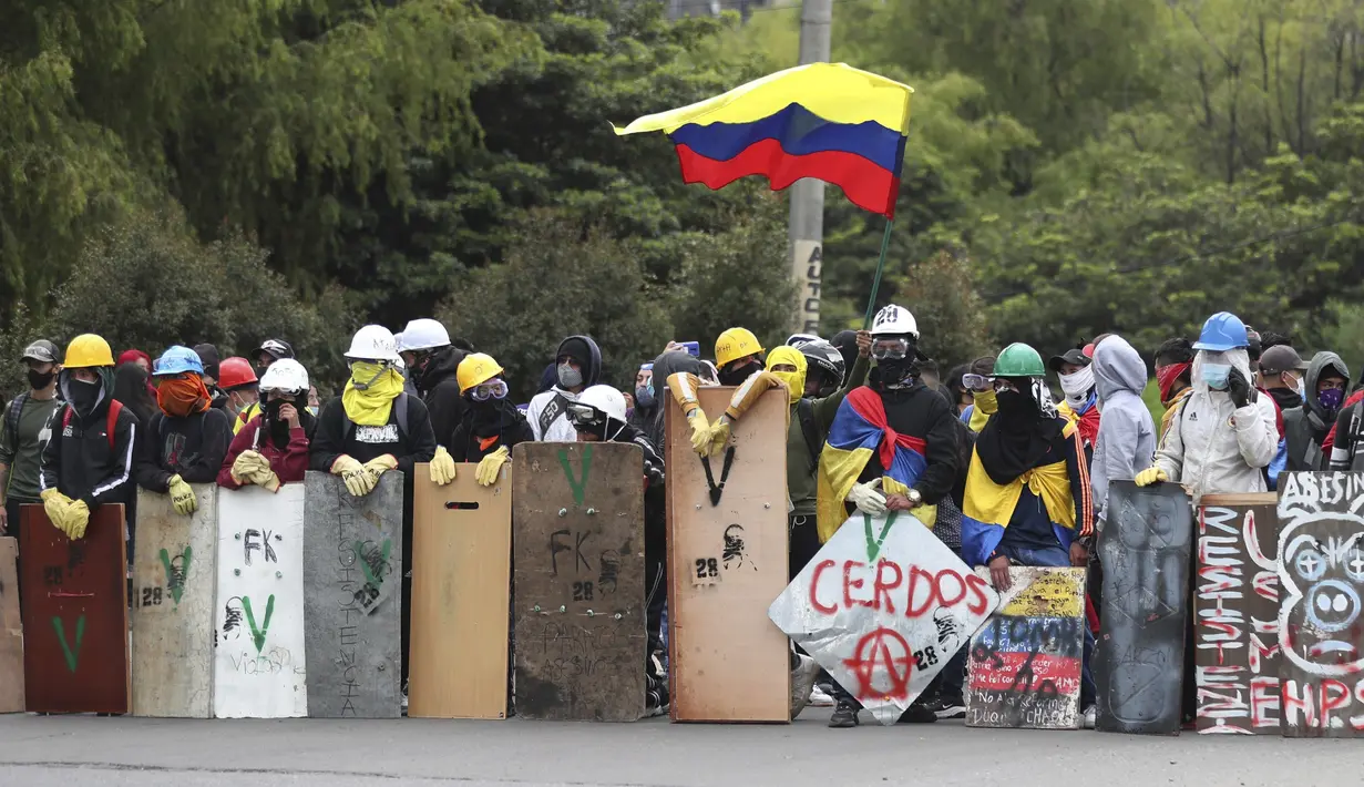 Pengunjuk rasa berdiri dengan perisai sambil mengibarkan bendera Kolombia di sekitar barikade yang terbakar selama protes anti-pemerintah di Bogota (28/5/2021). Warga Kolombia telah turun ke jalan selama berminggu-minggu setelah pemerintah mengusulkan kenaikan pajak. (AP Photo/Ivan Valencia)