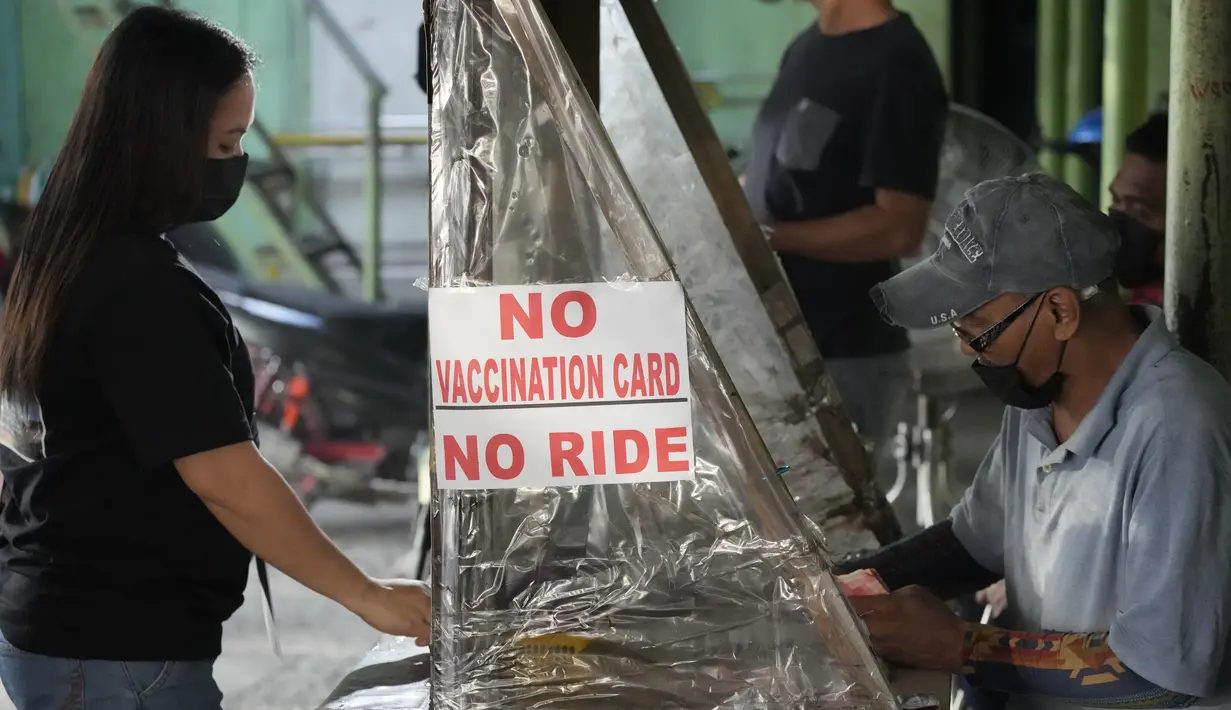 Seorang wanita berdiri dekat tanda yang mengingatkan penumpang untuk menunjukkan kartu vaksinasi sebelum naik di terminal jeepney di kota Quezon, Filipina, Senin (17/1/2022). Orang-orang yang belum menerima vaksin COVID-19 dilarang naik transportasi publik di ibu kota Manila. (AP Photo/Aaron Favila)
