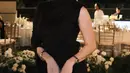 Elina Joerg tampil mengenakan dress hitam model lengan sleeveless dan long sleeves pada sisi lainnya. Dress kerah tinggi dipadukan handbag putih. [@elinaaaaajoerg]