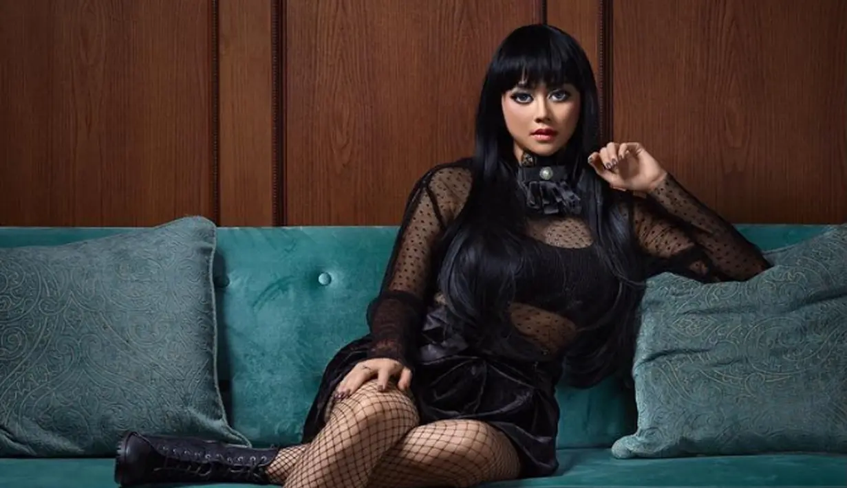 Artis Aura Kasih tampil seksi dengan bergaya gothic duduk di sebuah sofa hijau. Dengan balutan usan serba hitam, Aura Kasih terlihat sangat berbeda dari biasanya. (Instagram/rockyjaya)
