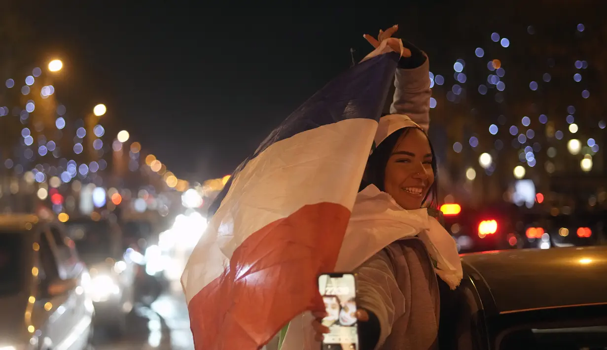 Suporter membawa bendera Prancis di jalan Champs Elysees usai kemenangan pertandingan semifinal Piala Dunia 2022 melawan Maroko, di Paris, Kamis (15/12/2022). Prancis berhasil mengalahkan Maroko dengan skor 2-0 dan melaju ke babak final menghadapi Argentina. (AP Photo/Thibault Camus)