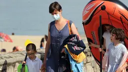 Seorang wanita mengenakan masker berjalan dengan anak-anaknya di sepanjang pantai di Saint Jean de Luz, Prancis barat daya, Selasa (27/7/2021). Otoritas setempat di Prancis memberlakukan kembali mandat masker karena penyebaran varian delta menyebabkan rawat inap meningkat lagi. (AP/Bob Edme)
