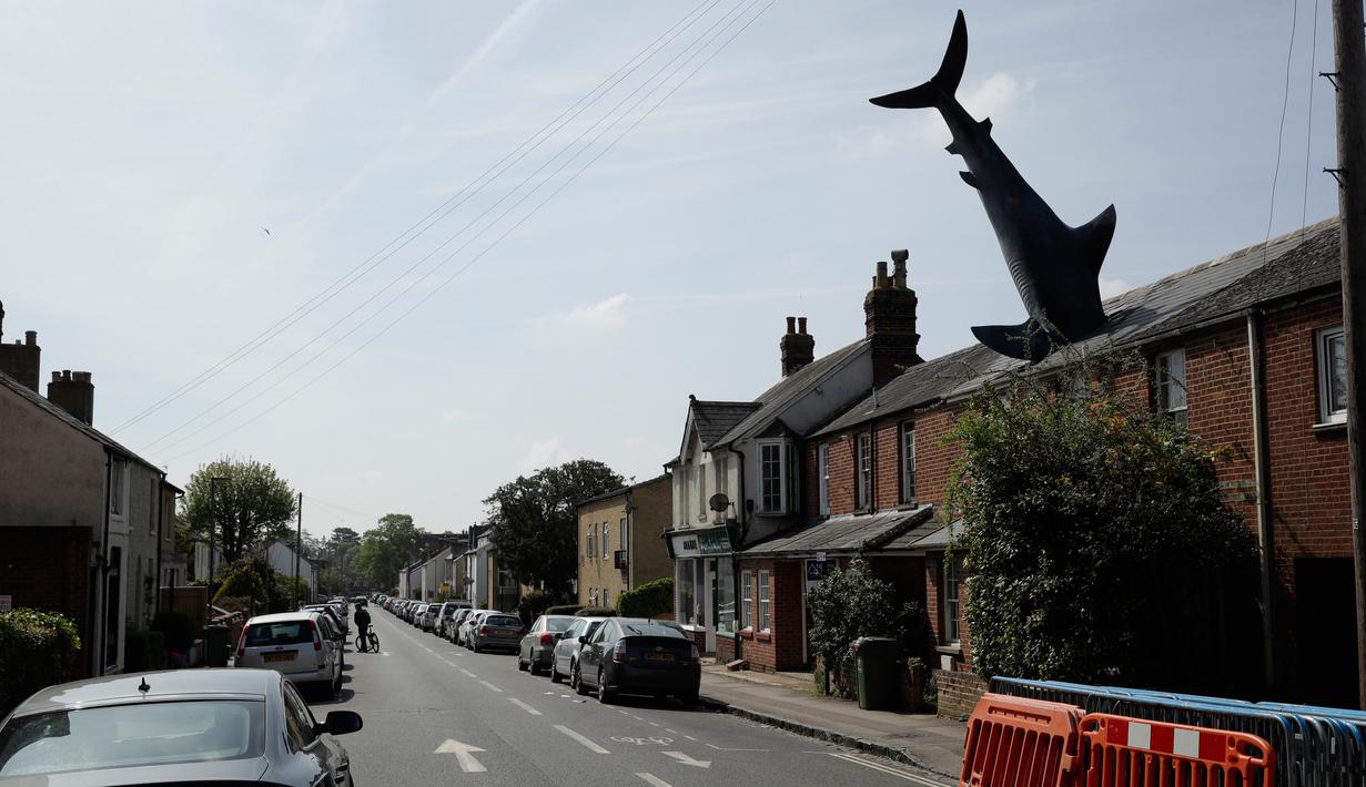 Patung dengan nama Headington Shark tampak menerobos atap rumah di wilayah pinggiran Oxford, Inggris pada 30 April 2019. Bagian kepalanya tidak terlihat karena dibuat seakan masuk ke dalam atap, sedangkan badan hingga ekornya menjulang ke langit dengan posisi terbalik.  (AP Photo/Matt Dunham)
