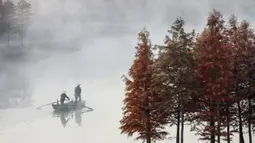 Warga mengendarai perahu di Danau Tianquan yang berselimut kabut di Xuyi di Provinsi Jiangsu, China (20/11/2019). Memasuki musik dingin, pemandangan Danau Tianquan berselimut kabut tipis berpadu dengan pepohonan berdaun kemerahan terlihat lebih indah dari biasanya. (AFP Photo/Str)