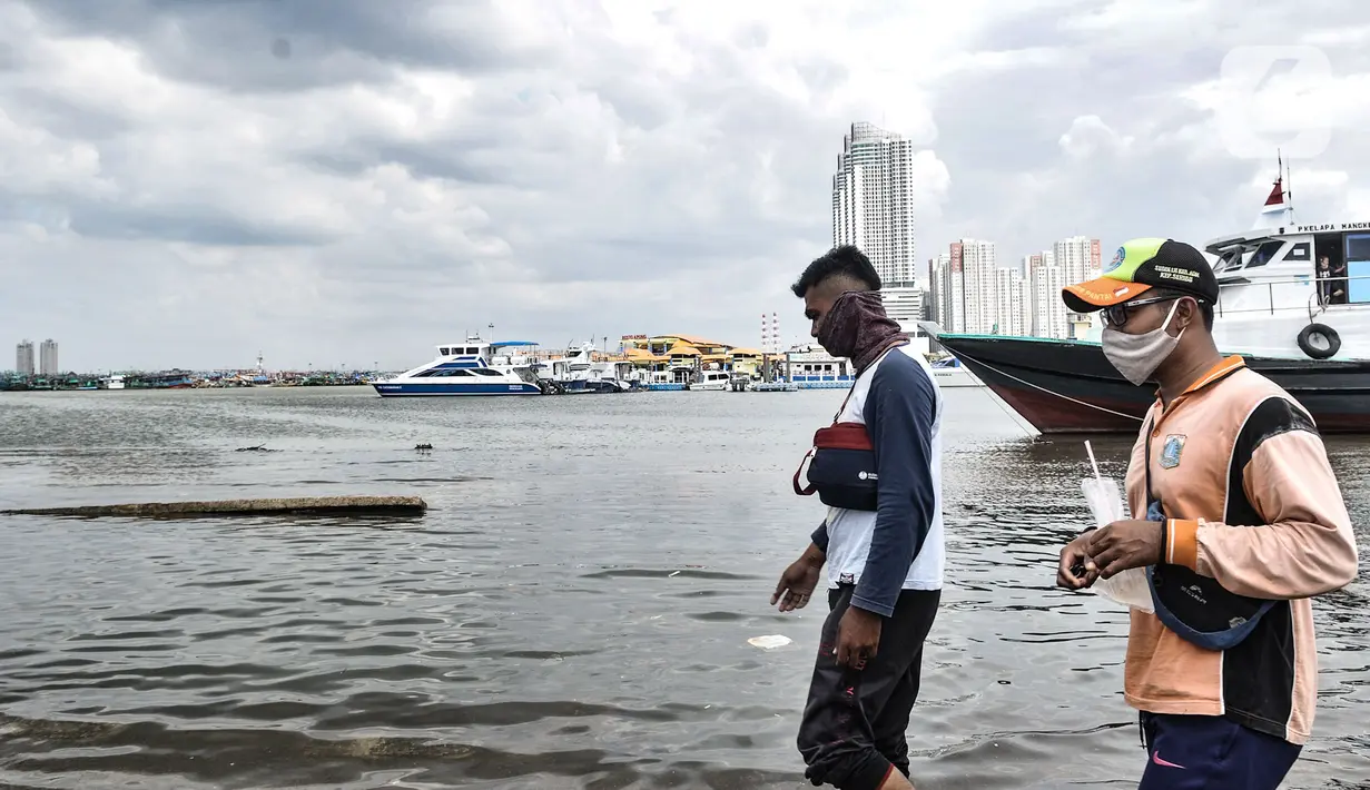 Petugas melintasi kapal yang tidak beroperasi saat banjir rob merendam Pelabuhan Kali Adem, Muara Angke, Jakarta, Kamis (22/10/2020). Banjir akibat air pasang dengan ketinggian mencapai 30 cm tersebut telah merendam kawasan Pelabuhan Kali Adem dan sudah berlangsung selama lima hari. (merdeka.com/Iqb