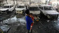 Seorang pria sambil menggendong anak melihat kondisi mobil yang hangus akibat kebakaran Depo Pertamina Plumpang, Koja, Jakarta Utara, Sabtu (4/3/2023). Kebakaran hebat melanda Depo Pertamina Plumpang pada Jumat malam, 3 Maret 2023. (merdeka.com/Arie Basuki)