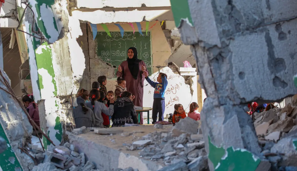 Foto yang dipublikasikan pada 4 Desember 2024 menunjukkan seorang guru Palestina, Doha al-Attar (30) saat memberi pelajaran kepada anak-anak di sebuah ruang kelas yang rusak parah di Khan Yunis, wilayah selatan Jalur Gaza. (Bashar TALEB/AFP)