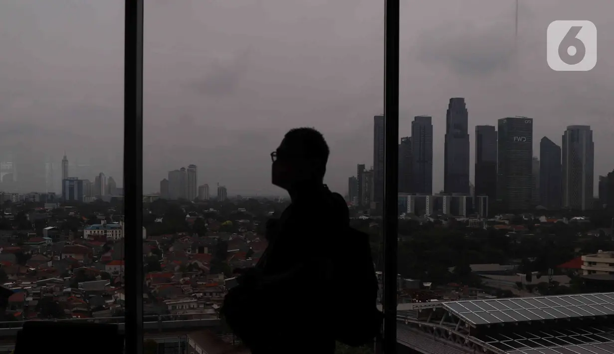 Seseorang melintas dekat jendela berlatar gedung bertingkat dan permukiman di kawasan Jakarta, Senin (17/1/2022). Bank Dunia memproyeksikan pertumbuhan ekonomi Indonesia pada tahun 2022 mencapai 5,2 persen. (Liputan6.com/Angga Yuniar)