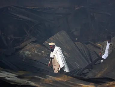 Dua pria berjalan di antara reruntuhan setelah kebakaran menghanguskan pasar peralatan elektronik di Kabul, Afghanistan (2/11). Warga ibukota Afghanistan bergulat memadamkan kobaran api besar yang menghancurkan ratusan toko. (AP Photo/Massoud Hossaini)