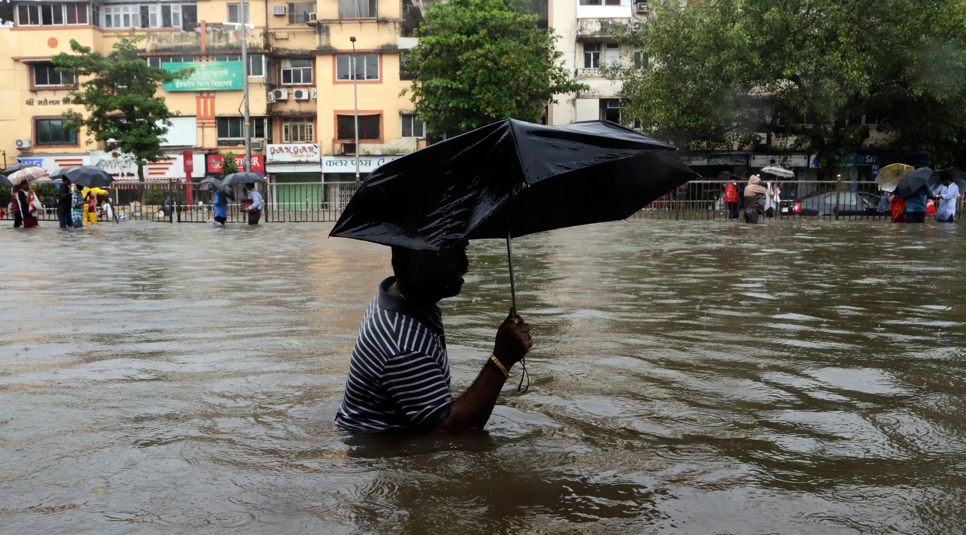 Seorang pria menggunakan payung sambil berjalan melewati banjir yang merendam kota Mumbai, India, Selasa (29/8). Hujan lebat yang terus-menerus mengguyur Mumbai mengakibatkan banjir di beberapa daerah di kota tersebut. (AP Photo/Rajanish Kakade)