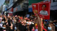 Seorang pengunjuk rasa memegang poster dengan gambar pemimpin terpilih Aung San Suu Kyi (kanan) yang ditahan dan presiden Win Myint saat demonstrasi menentang kudeta militer di Yangon, Myanmar pada Sabtu (6/2/2021).  Ribuan orang turun ke jalan-jalan untuk melawan kudeta. (YE AUNG THU / AFP)