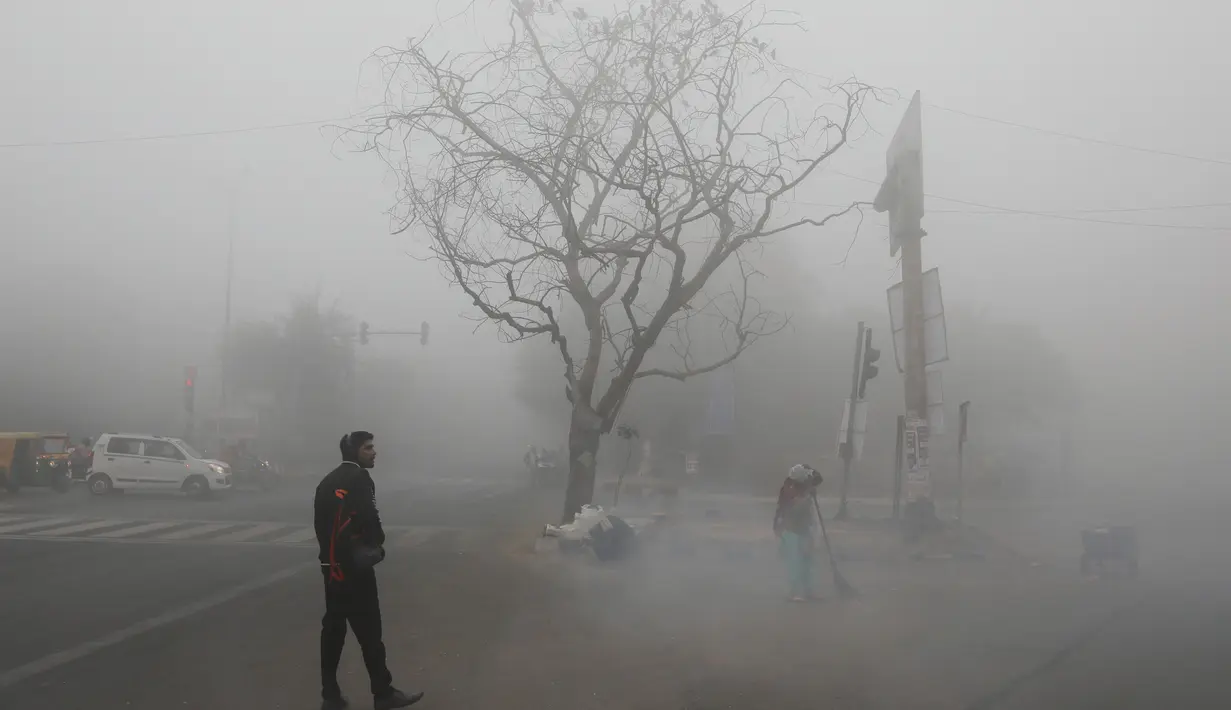 Seseorang melintasi persimpangan ketika petugas menyapu jalan di tengah kabut tebal di New Delhi, Senin (30/12/2019). New Delhi, ibu kota India, saat ini mengalami musim dingin dengan hari dingin terpanjang dalam 22 tahun terakhir. (AP Photo/Manish Swarup)