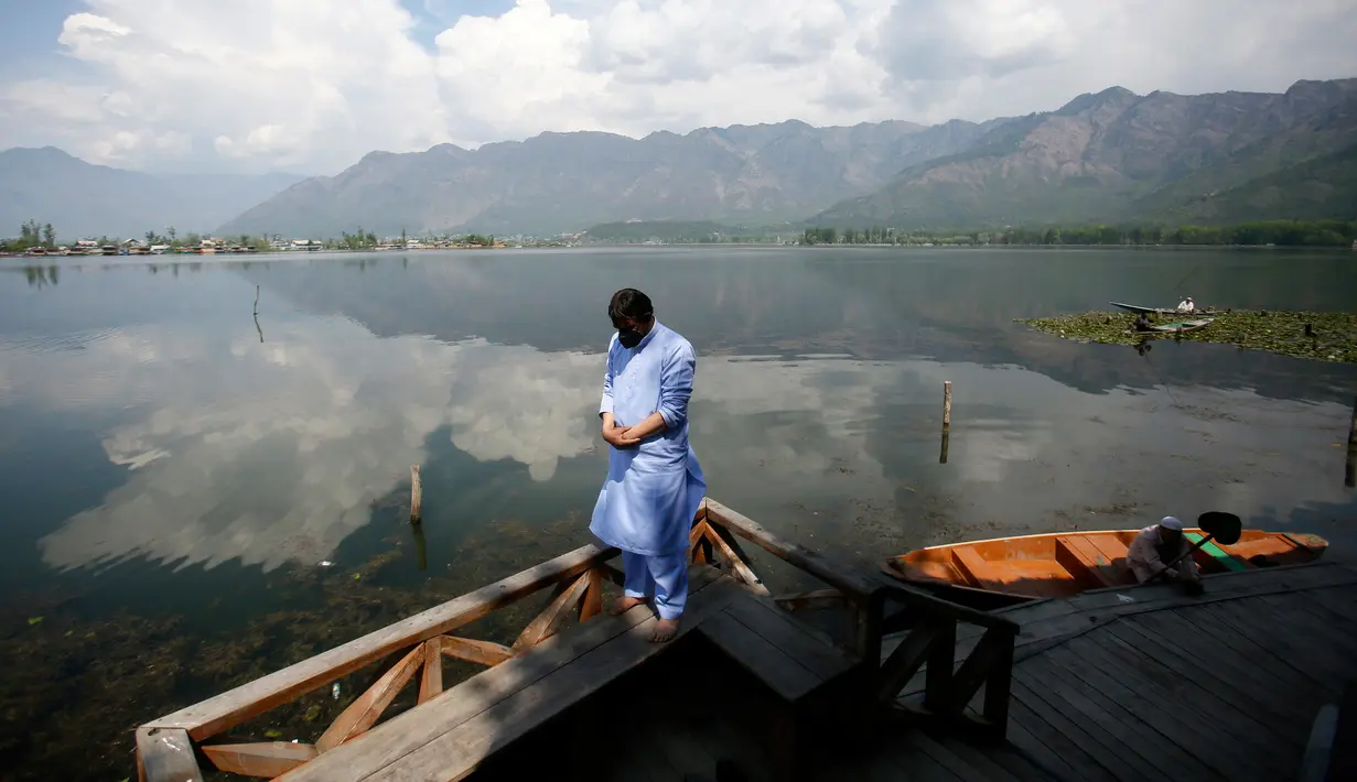 Seorang pria Muslim Kashmir melaksanakan salat di tepi Danau Dal pada hari kedua Ramadan selama penguncian nasional untuk mengendalikan penyebaran virus corona Covid-19, di Srinagar, Kashmir yang dikuasai India, (26/4/2020). (AP Photo/Mukhtar Khan)