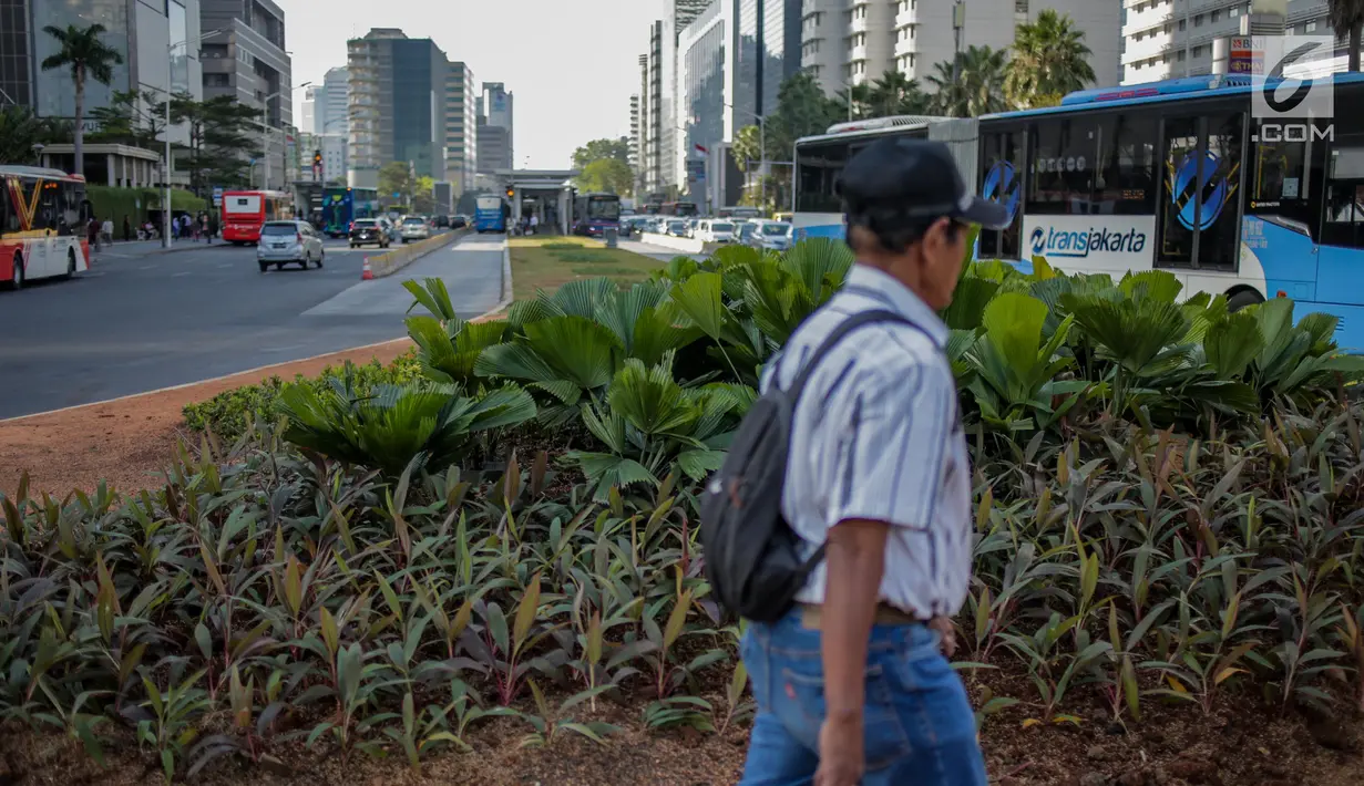 Pejalan kaki melintasi jalur hijau usai pembongkaran instalasi bambu Getah Getih di Bundaran HI, Jakarta, Kamis (18/7/2019). Masyarakat kini bisa melihat jelas Monumen Selamat Datang dari halte transjakarta Bundaran HI tanpa terhalang karya seni bernilai Rp550 juta itu. (Liputan6.com/Faizal Fanani)