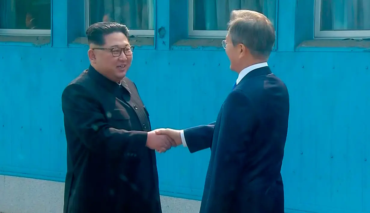 Presiden Korea Selatan, Moon Jae-in menyambut kedatangan Pemimpin Korea Utara, Kim Jong-un di Zona Demiliterisasi (DMZ), Panmunjom, Jumat (27/4). Keduanya berjabat tangan sambil menempatkan senyum di bibir masing-masing. (Korea Broadcasting System via AP)