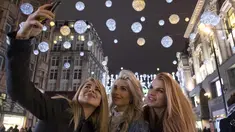 Tiga wanita berswafoto di bawah lampu Natal di Oxford Street, di pusat kota London, Inggris (5/12). (AFP Photo/Justin Tallis)