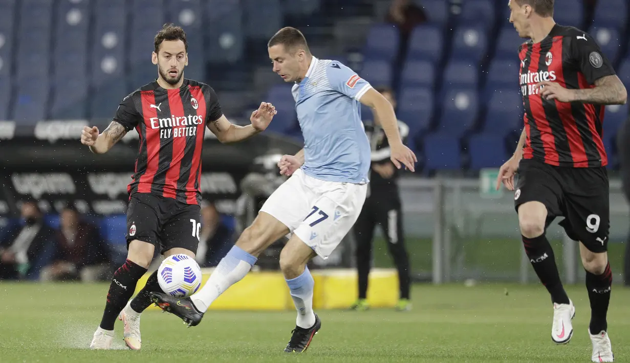 Gelandang AC Milan, Hakan Calhanoglu bersaing memperebutkan bola dengan bek Lazio, Adam Marusic dalam laga pekan ke-33 Liga Italia 2020-2021 di Stadio Olimpico, Selasa dinihari WIB (27/4/2021). AC Milan kalah telak 3-0 saat menyambangi kandang Lazio. (AP Photo/Gregorio Borgia)