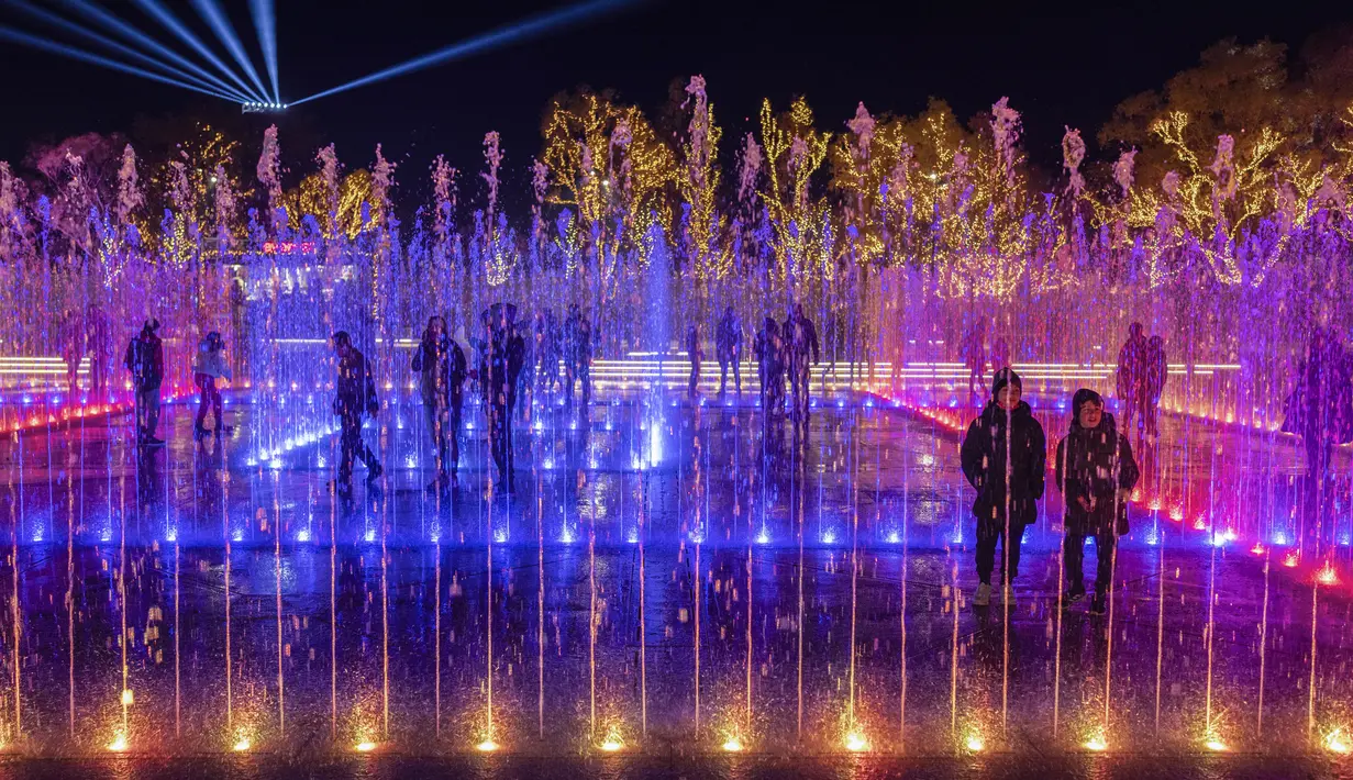 Orang-orang berdiri di dalam pertunjukan cahaya Natal dan tampilan air mancur yang disinkronkan di Experience Park, di distrik pesisir Hellenikon, Athena, Senin (20/12/2021). (AP Photo/Petros Giannakouris)