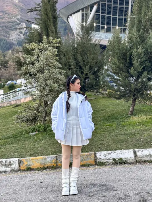 Fuji tampil dengan outfit serba putih. Ia mengenakan turtleneck putih dipadu dengan pleated skirt, legging transparan, kaus kaki panjang, dan sneakers, serta sunglasses dengan frame yang semuanya berwarna putih. [Foto: Instagram/fuji_an]
