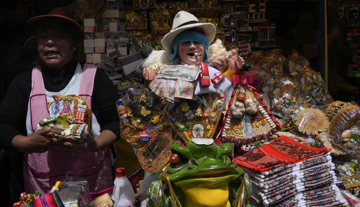 Seorang perempuan menjual barang-barang miniatur di samping patung Ekeko, Dewa Kemakmuran, pada hari pembukaan Pameran tahunan Alasita, di mana Ekeko adalah tokoh utamanya di El Alto, Bolivia, Selasa (24/1/2023). Orang-orang membeli replika kecil dari hal-hal yang ingin mereka peroleh sepanjang tahun, seperti rumah, mobil, dan kekayaan. Kata Aymara "Alasita" berarti "belikan aku". (AP Photo/Juan Karita)