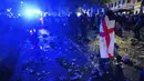 Seorang suporter menenteng bendera nasional Inggris berjalan diantara sampah yang berserakan di Kota London paska final Euro 2020 antara Timnas Inggris melawan Italia. (Foto:AP/Victoria Jones)