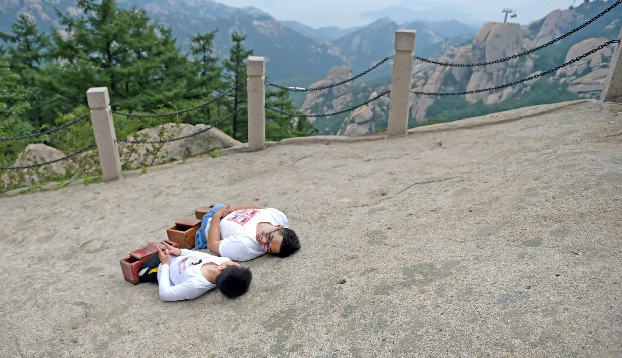 Gao Zhiyu (kiri) dan Chen Zhou merebahkan dirinya saat sampai di puncak gunung di Qingdao, Tiongkok, Selasa (13/9). Keduanya tak memiliki kaki dan menggunakan balok kayu untuk mendaki gunung setinggi 1130 meter. (REUTERS)