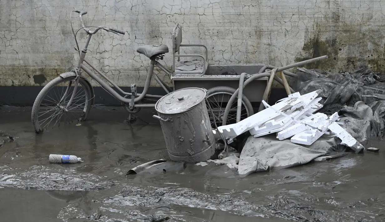 Sebuah sepeda roda tiga yang tertutup lumpur terlihat di dekat rumah seorang warga setelah banjir akibat hujan lebat di kota Zhuozhou, di provinsi Hebei, China utara, Rabu (9/8/2023). (Jade Gao / AFP)