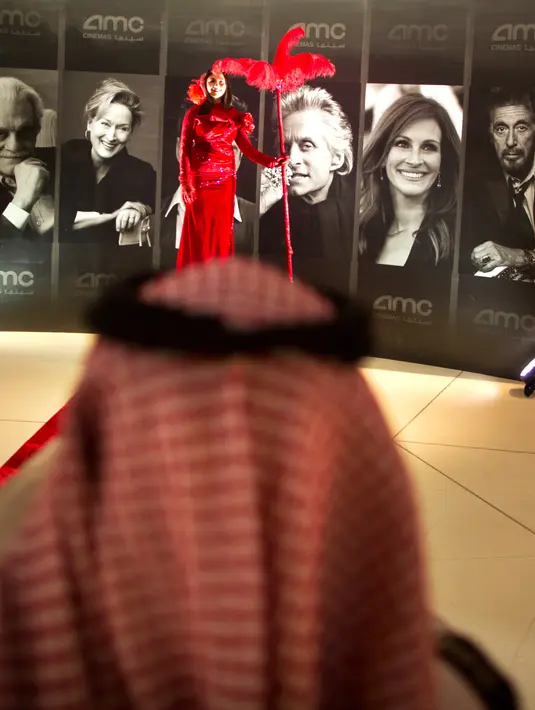 Seorang wanita berpose di depan poster bintang Hollywood selama acara gala undangan di King Abdullah Financial District Theatre, ibu kota Riyadh, Rabu (18/4). Setelah pelarangan selama 35 tahun, bioskop kembali beroperasi di Arab Saudi. (AP/Amr Nabil)