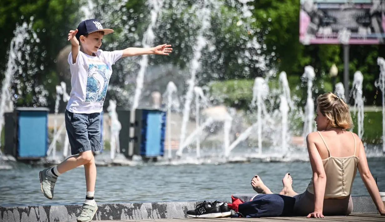 Orang-orang menikmati musim semi yang panas dengan bermain dekat air mancur di Moskow, Rusia, Selasa (18/5/2021). Suhu di Moskow telah mencapai 31 derajat Celcius. (Alexander NEMENOV/AFP)