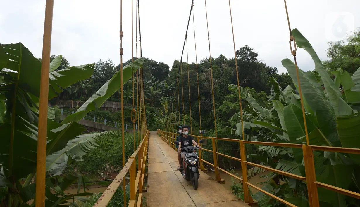 Pengendara motor melintasi jembatan gantung Kuning yang menghubungkan Pasar Minggu Poltangan ke Cililitan Condet, Jakarta, Selasa (28/12/2021). Jembatan gantung dengan panjang 40 meter di atas sungai Ciliwung tersebut baru baru ini dijadikan lokasi foto untuk konten medsos. (merdeka.com/Imam Buhori)