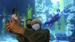 Pengunjung yang mengenakan masker untuk mencegah COVID-19 berswafoto saat penyelam berkostum tradisional Korea tampil merayakan Tahun Baru dalam akuarium di Seoul, Korea Selatan, Minggu (3/1/2021). (AP Photo/Ahn Young-joon)