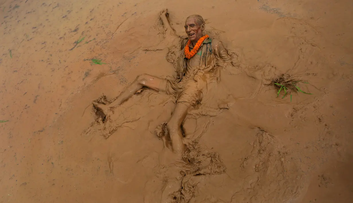 Seorang lelaki tua jatuh ke lumpur sawah saat merayakan Asar Pandra atau hari menanam padi di Distrik Dhading, Nepal, Minggu (30/6/2019). Umat Hindu Nepal menganggap Asar Pandra sebagai hari baik untuk menanam padi. (AP Photo/Niranjan Shrestha)