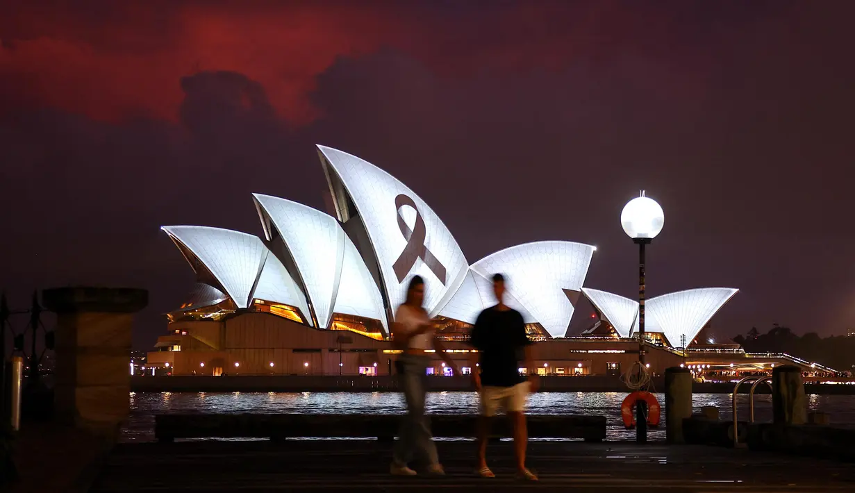 Anggota masyarakat berjalan melewati pita hitam yang melambangkan kenangan dan duka cita diproyeksikan ke Sydney Opera House pada 9 Februari 2023 sebagai bentuk solidaritas terhadap Turki dan Suriah setelah gempa bumi dahsyat meluluhlantakkan kedua negara tersebut. (DAVID GRAY/AFP)