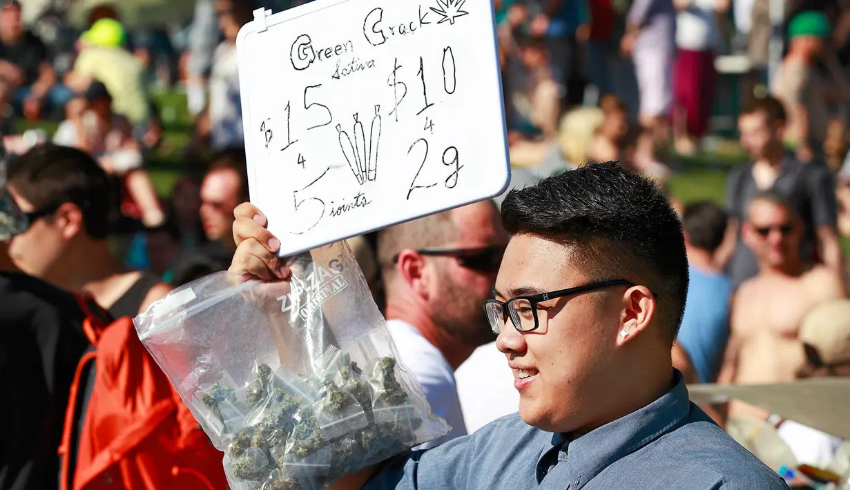Seorang pria menjual ganja saat ribuan orang berkumpul dalam acara legalisasi ganja 4/20 di Vancouver, Kanada (20/4). Ribuan orang menghisap ganja diruang terbuka dalam acara festival Vancouver 4/20. (AFP/Jeff Vinnick)