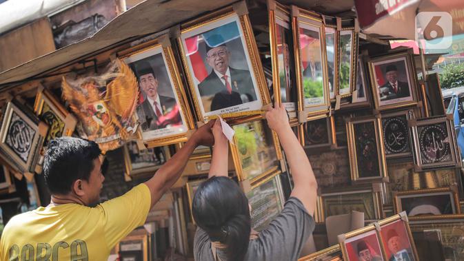 Pedagang melayani pembeli bingkai foto Presiden Jokowi dan Wakil Presiden terpilih Ma'ruf Amin yang dijualnya di Pasar Baru, Jakarta, Rabu (16/10/2019). Menjelang pelantikan presiden, foto pasangan Jokowi-Ma'ruf Amin mulaih dijual ke pasar umum. (Liputan6.com/Faizal Fanani)