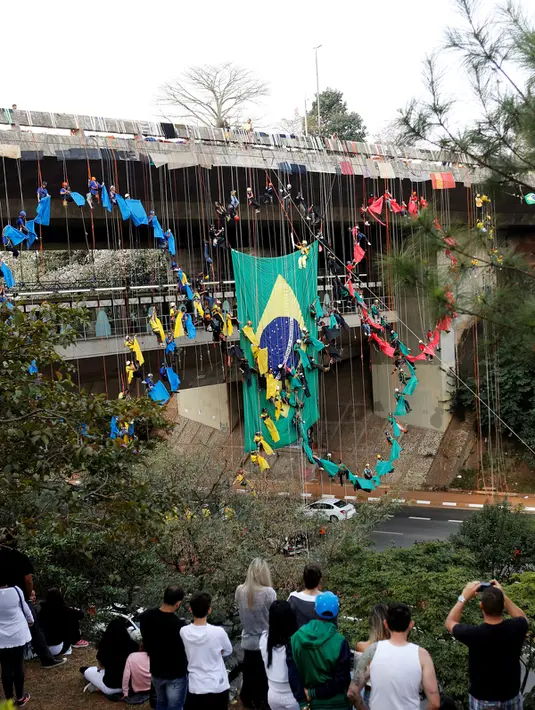 Sejumlah warga menyaksikan para pendaki profesional membuat cincin Olimpiade 2016 di sebuah jembatan di Sao Paulo, Brasil (31/7). Aksi ini dilakukan untuk menyambut dan memeriahkan Olimpiade 2016. (REUTERS/Paulo Whitaker) 
