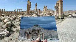 Seorang fotografer memegang foto Arc du Triomphe yang diambil pada tanggal 14 Maret 2014 di depan sisa-sisa kuil bersejarah setelah dihancurkan oleh ISIS pada Oktober 2015 di kota kuno Palmyra, Suriah, 31 Maret 2016. (Joseph EID/AFP)