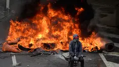Seorang demonstran dari oposisi Venezuela duduk didepan kobaran api saat menggelar aksinya menentang Presiden Nicolas Maduro di Caracas, Venezuela (24/4). Mereka menggelar protes meminta Presiden Nicolas Maduro untuk mundur. (AFP/Federico Parra)