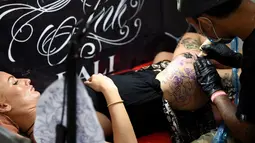 Seorang wanita saat dibuatkan tato dibagian pahanya oleh seniman dalam acara Bali Tattoo Expo 2017 di pulau resor Indonesia, Denpasar, Bali (12/5). Acara ini digelar selama 3 hari, mulai (12/5/2017) sampai (14/5/2017). (AFP Photo/Sonny Tumbelaka)