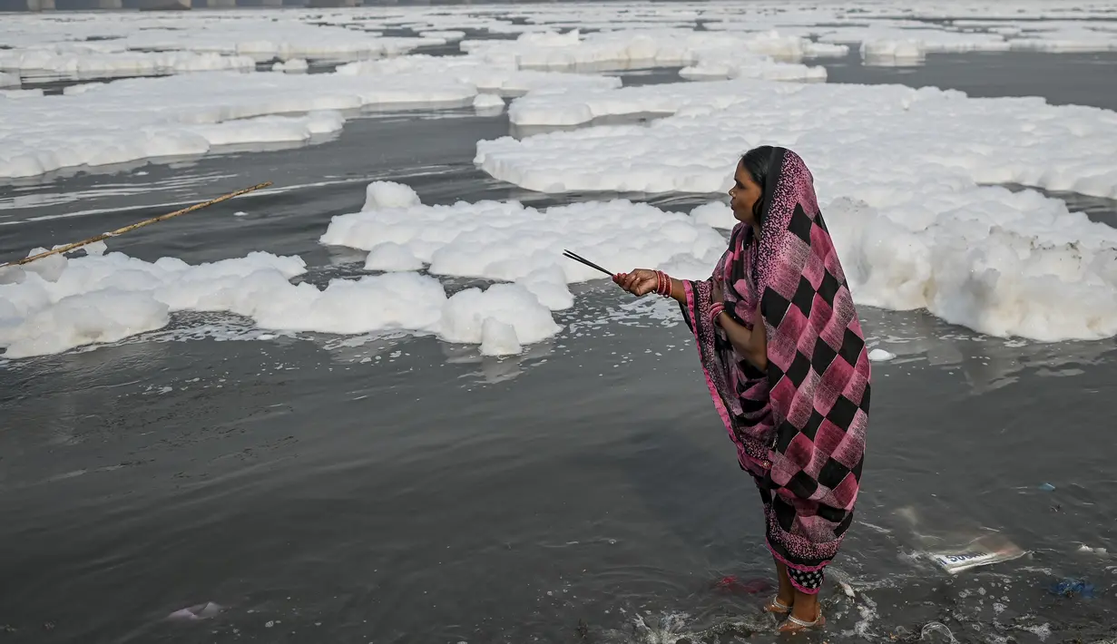 Sejumlah wanita berdoa di sungai Yamuna yang tertutup busa limbah sebagai bagian dari ritual untuk festival Chhath Puja yang akan datang di New Delhi, Senin (8/11/2021). Sungai yang sangat dianggap suci oleh umat Hindu India ini dipenuhi lapisan busa karena limbah beracun. (Sajjad HUSSAIN / AFP)